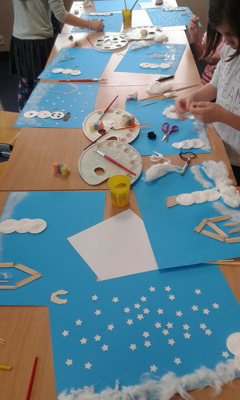 na ławkach są porozkładane prace które robią dzieci. Na niebieskim tle są wykonane z pomocą m.in. waty, wykałaczek i farb zimowe krajobrazy, bałwany