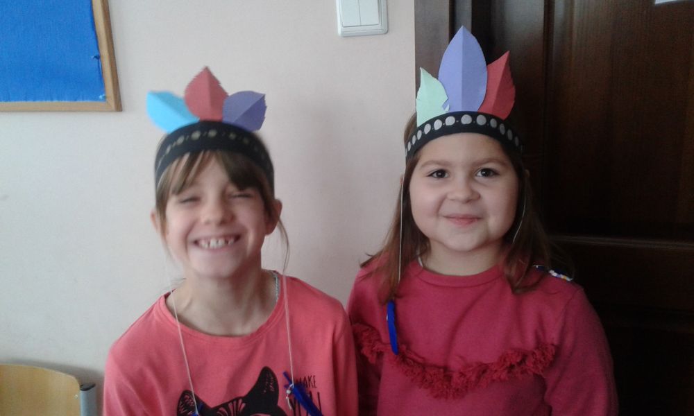 2 uśmiechnięte uczennice w wykonanych własnoręcznie pióropuszach na głowach