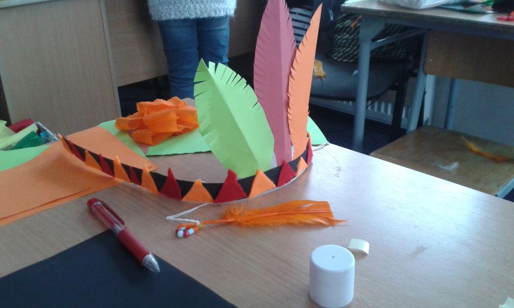 wykonany przez dziecko pióropusz indiański z przyklejonymi do opaski czerwonymi i pomarańczowymi trójkątami z filcu oraz wyciętymi z kolorowych kartek piórami