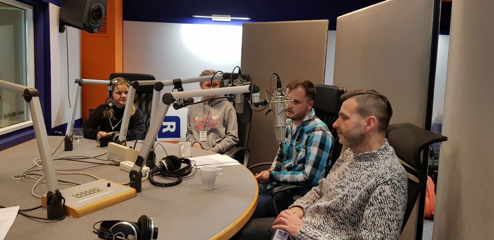 dyrektor szkoły, nauczyciel języka angielskiego i dwie uczennice siedzą w studio nagrań, przy mikrofonach