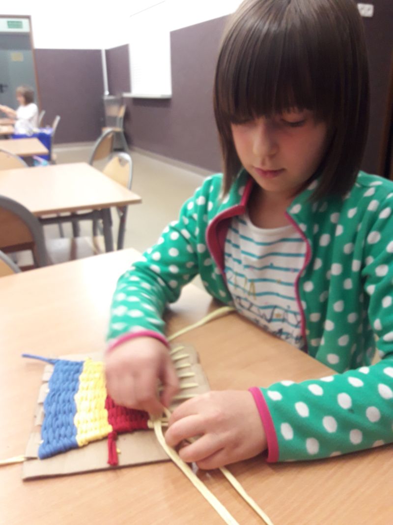 Uczennica klasy drugiej kończy wykonywać dywanik w trzech kolorach