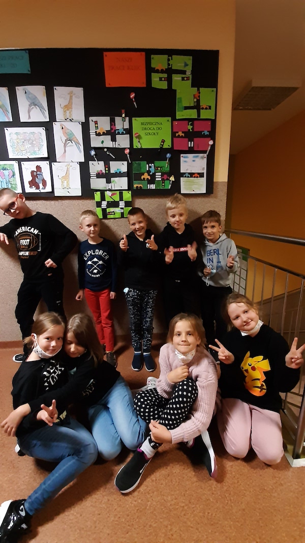 Zdjęcie przedstawia uczniów stojący przy tablicy z pracami o bezpiecznej drodze do szkoły. 