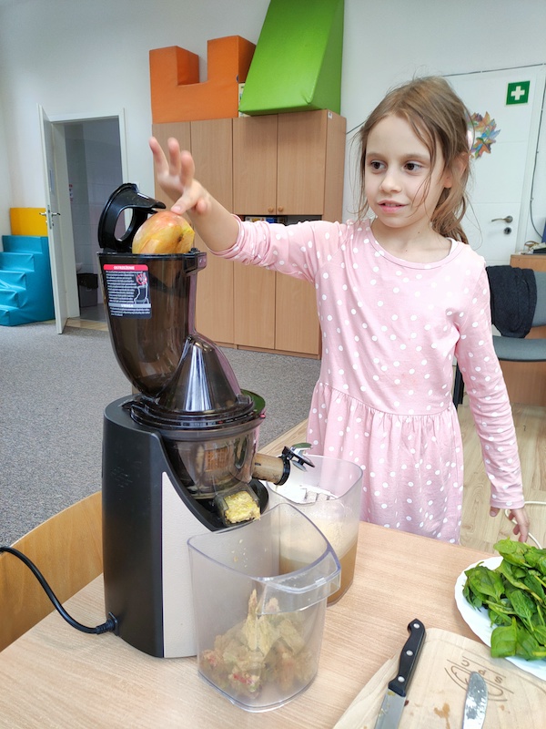 zdjęcie przedstawia dziewczynkę robiącą sok za pomocą wyciskarki