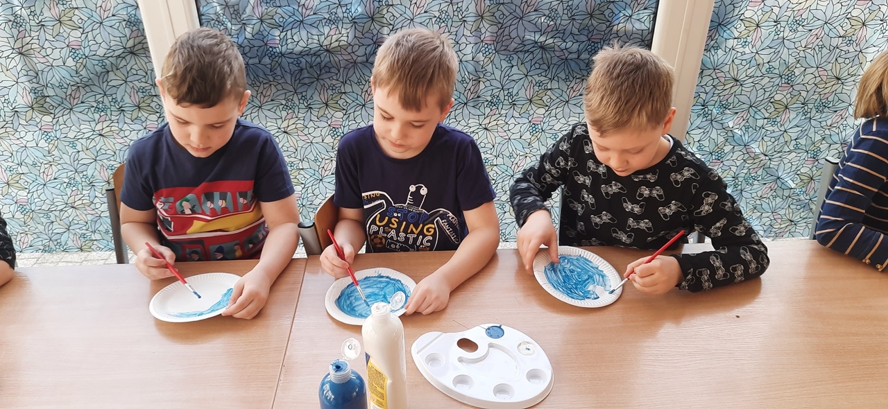chłopcy malujący niebieską farbą papierowe talerzyki, na których będą wyklejane przebiśniegi
