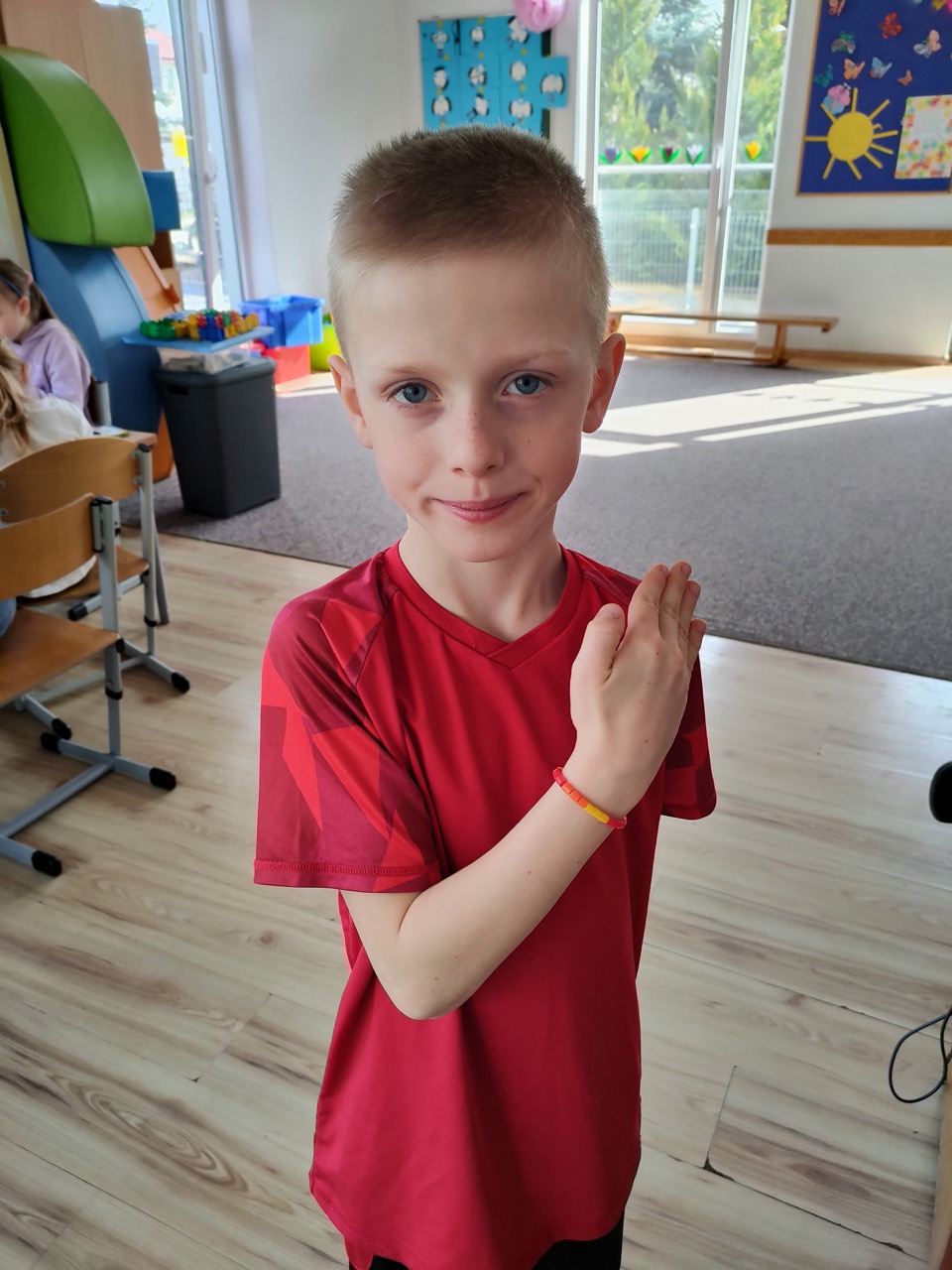 zdjęcie przedstawia chłopca prezentującego wykonaną przez siebie bransoletkę