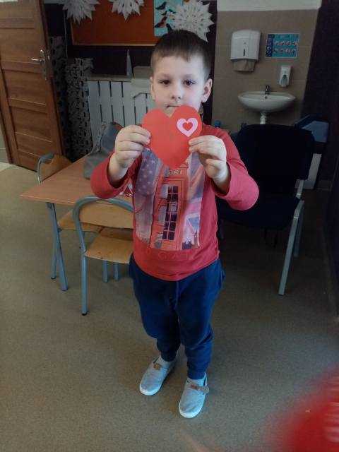 chłopiec prezentuje wykonaną przez siebie walentynkę z papieru kolorowego w kształcie serca 