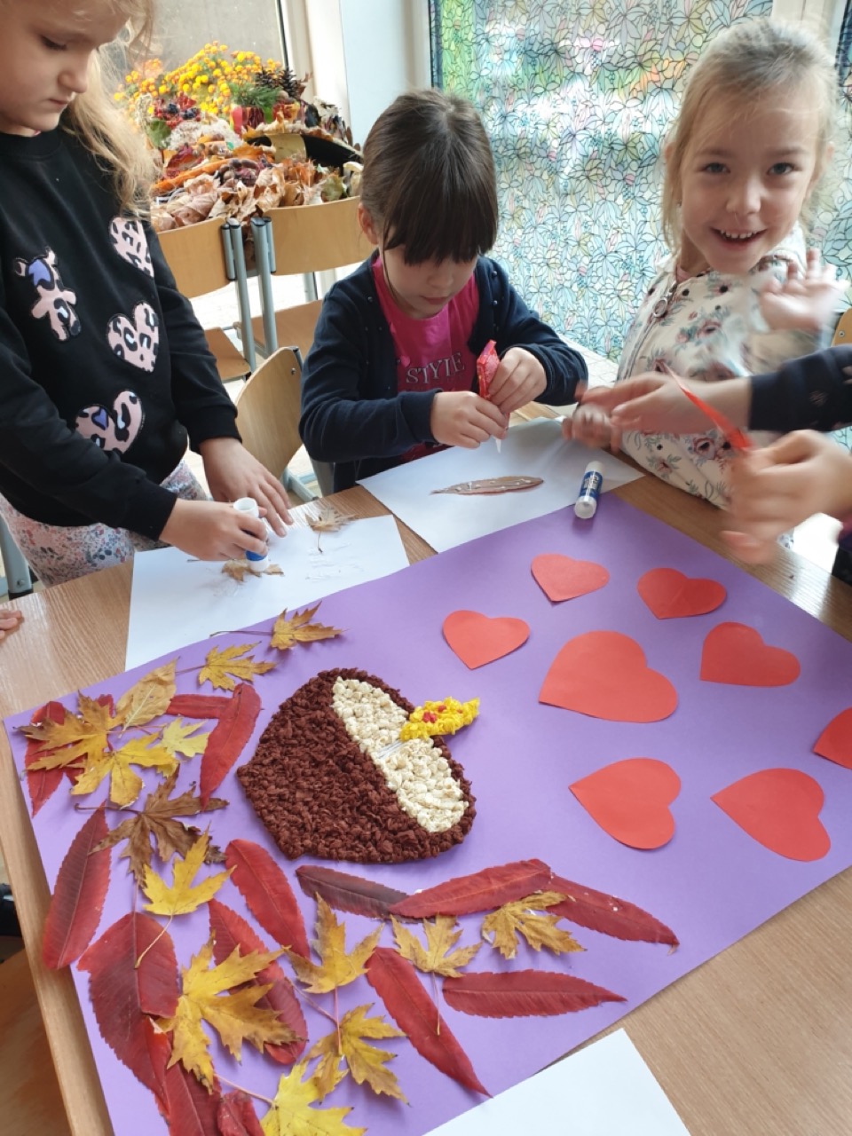 dzieci podczas pracy nad plakatem przedstawiającym znicz otoczony sercami