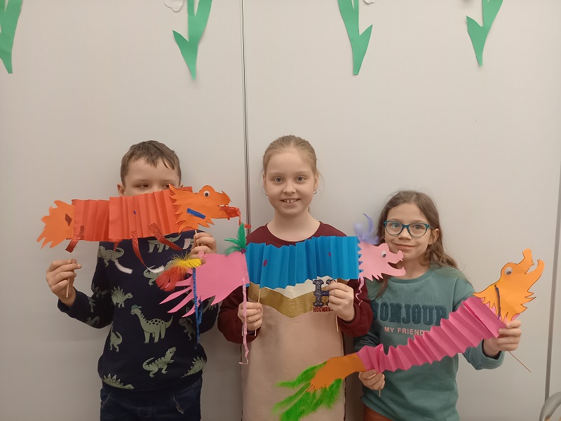 troje dzieci prezentuje wykonane przez siebie smoki chińskie