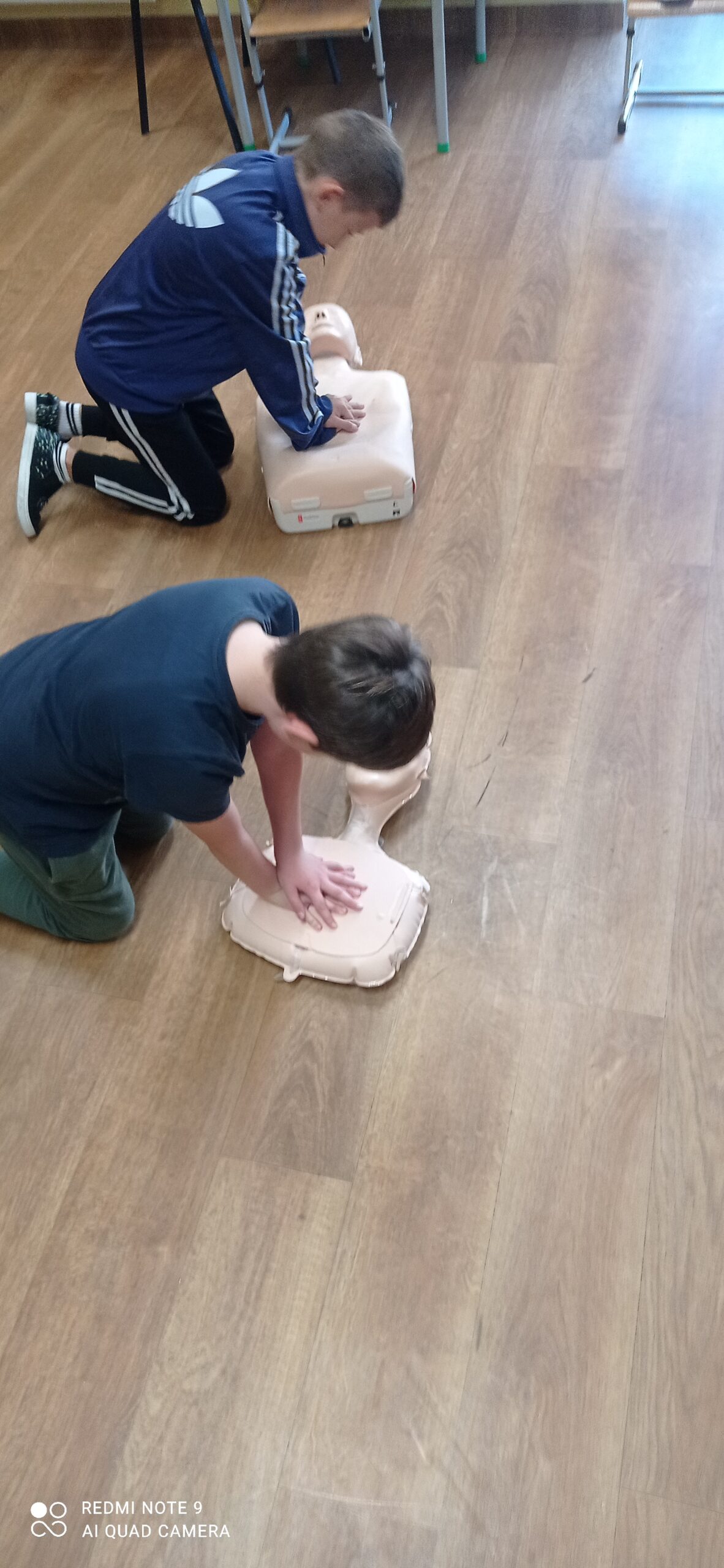 Zdjęcie przedstawia dwoje dzieci które klęcząc na podłodze ugniatają fantomy wykonując resuscytację