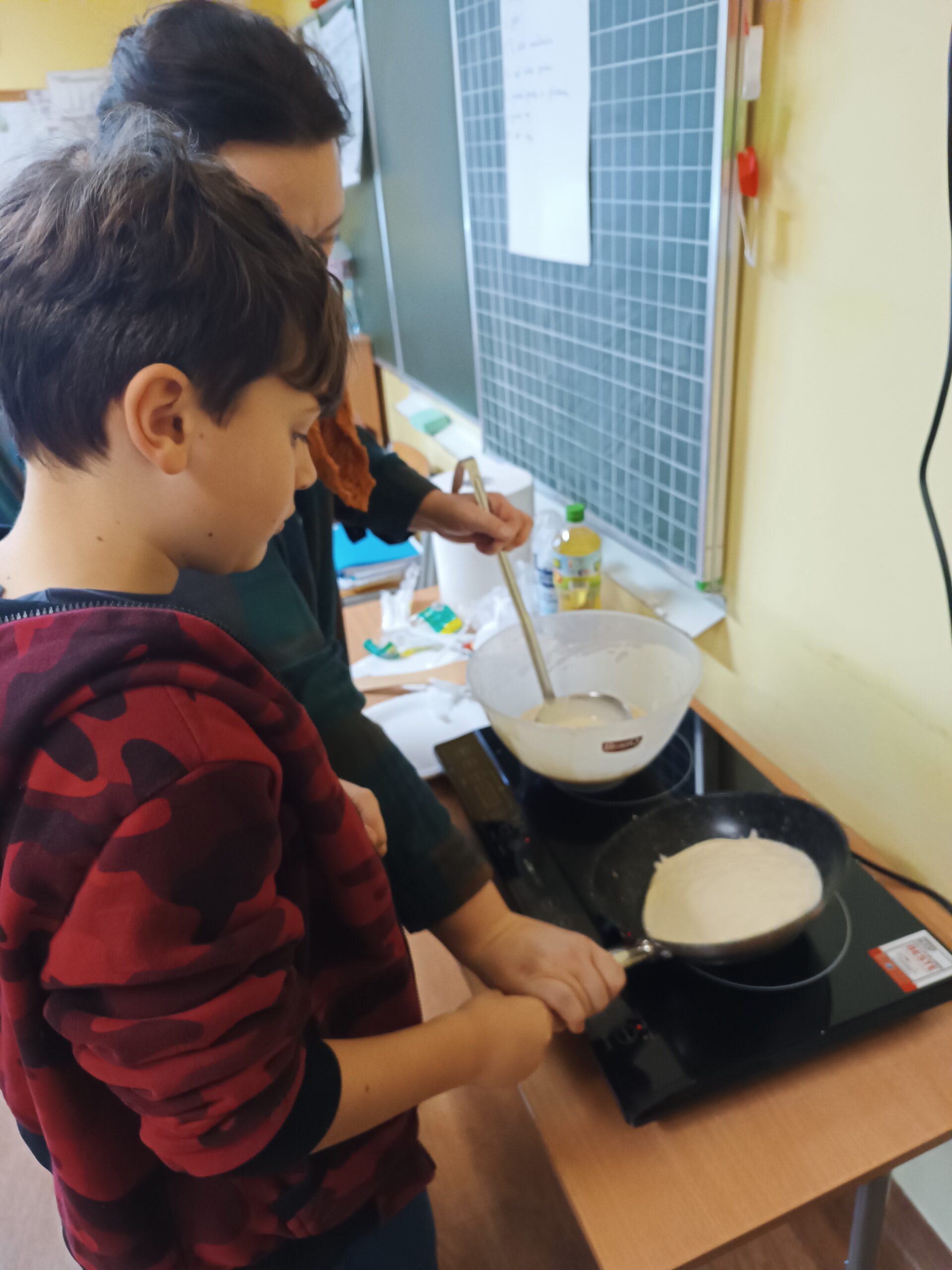 Na zdjęciu chłopiec smaży pancakes, rozprowadza ciasto na patelni