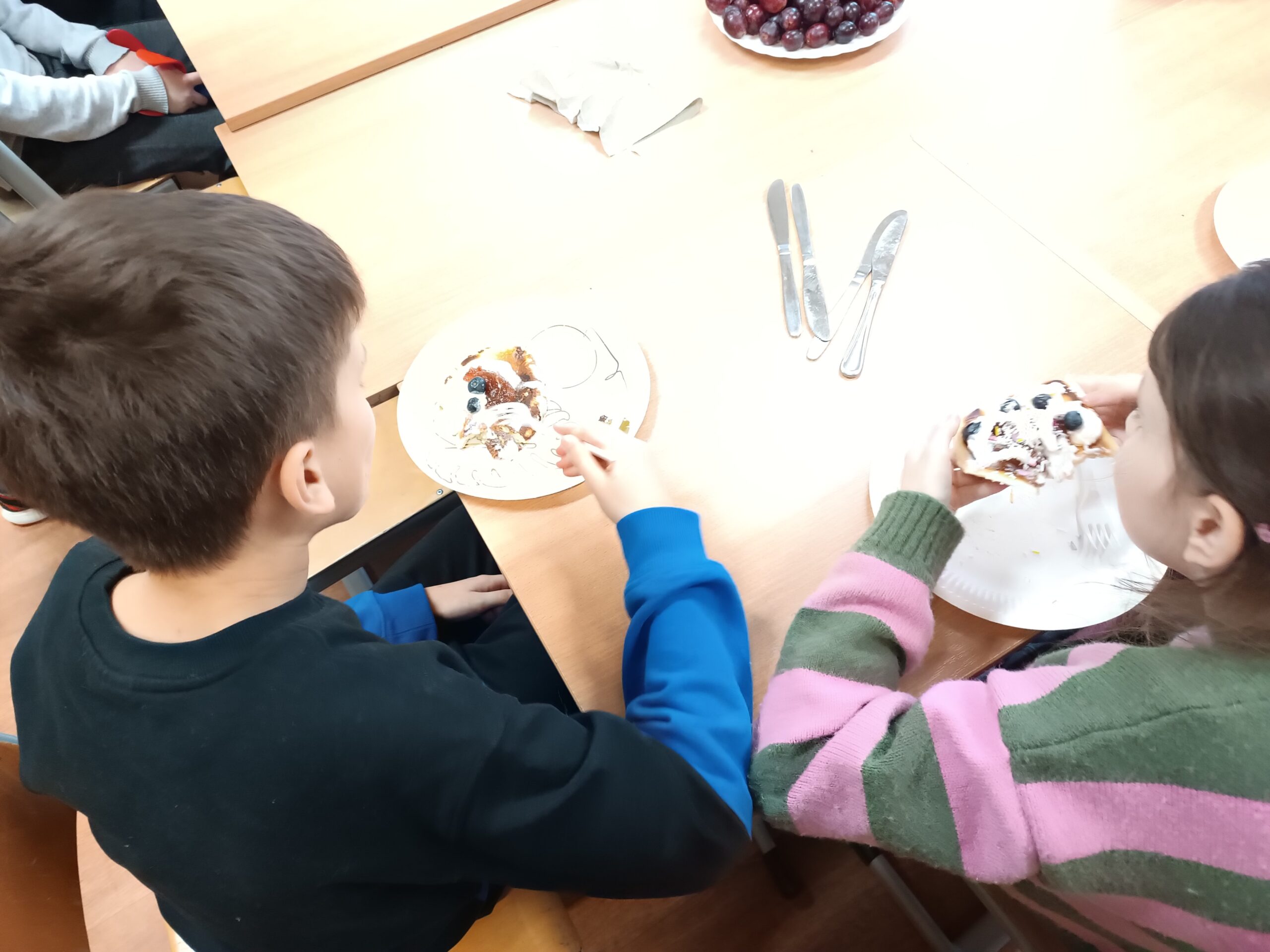 Na zdjęciu widać dzieci jedzące udekorowane owocami i śmietaną placuszki 