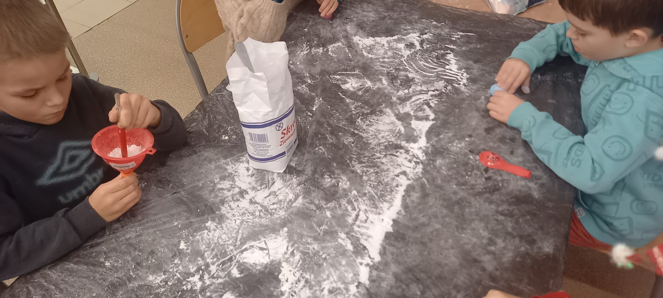 dzieci wykonują gniotki z balonów, wsypują do nich mąkę, chłopiec bawi się wykonanymi gniotkami