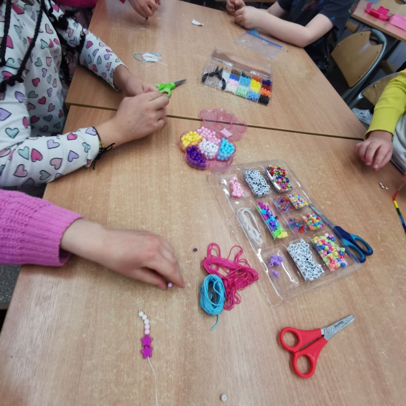 dzieci wykonują bransoletki z koralików nawlekają na gumki