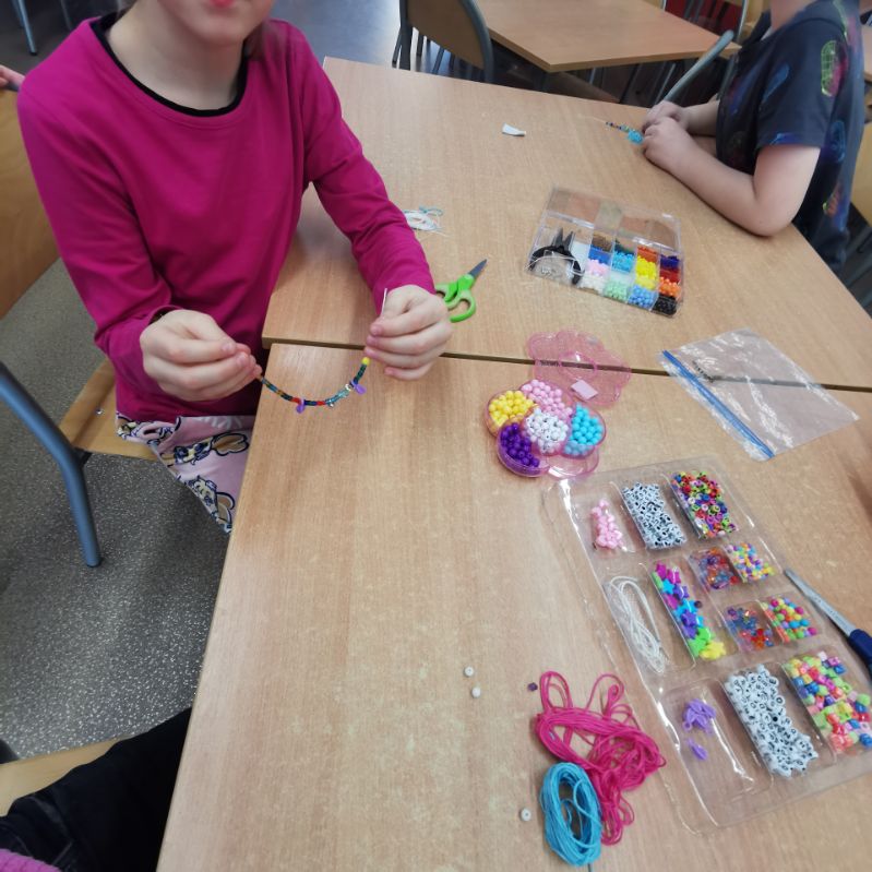 dzieci wykonują bransoletki z koralików nawlekają na gumki
