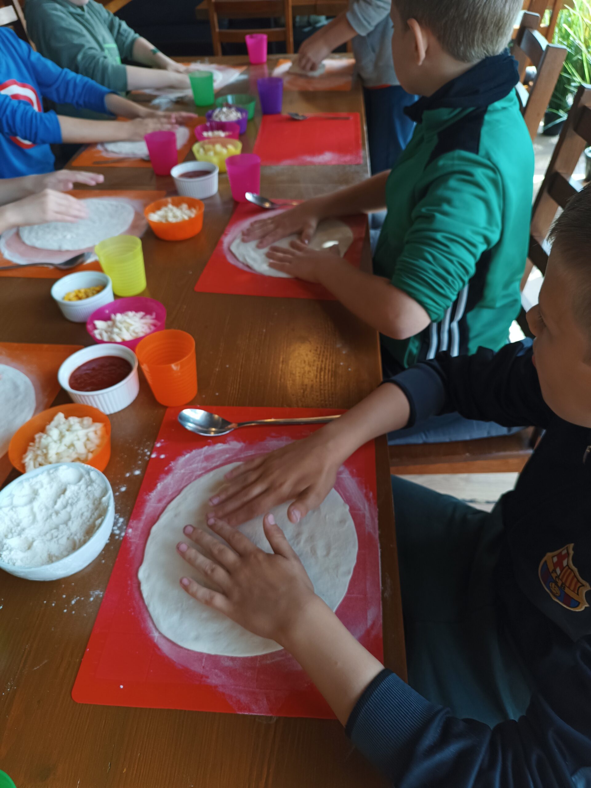 Na zdjęciu widać dzieci formułujące ciasto do pizzy w odpowiedni kształt