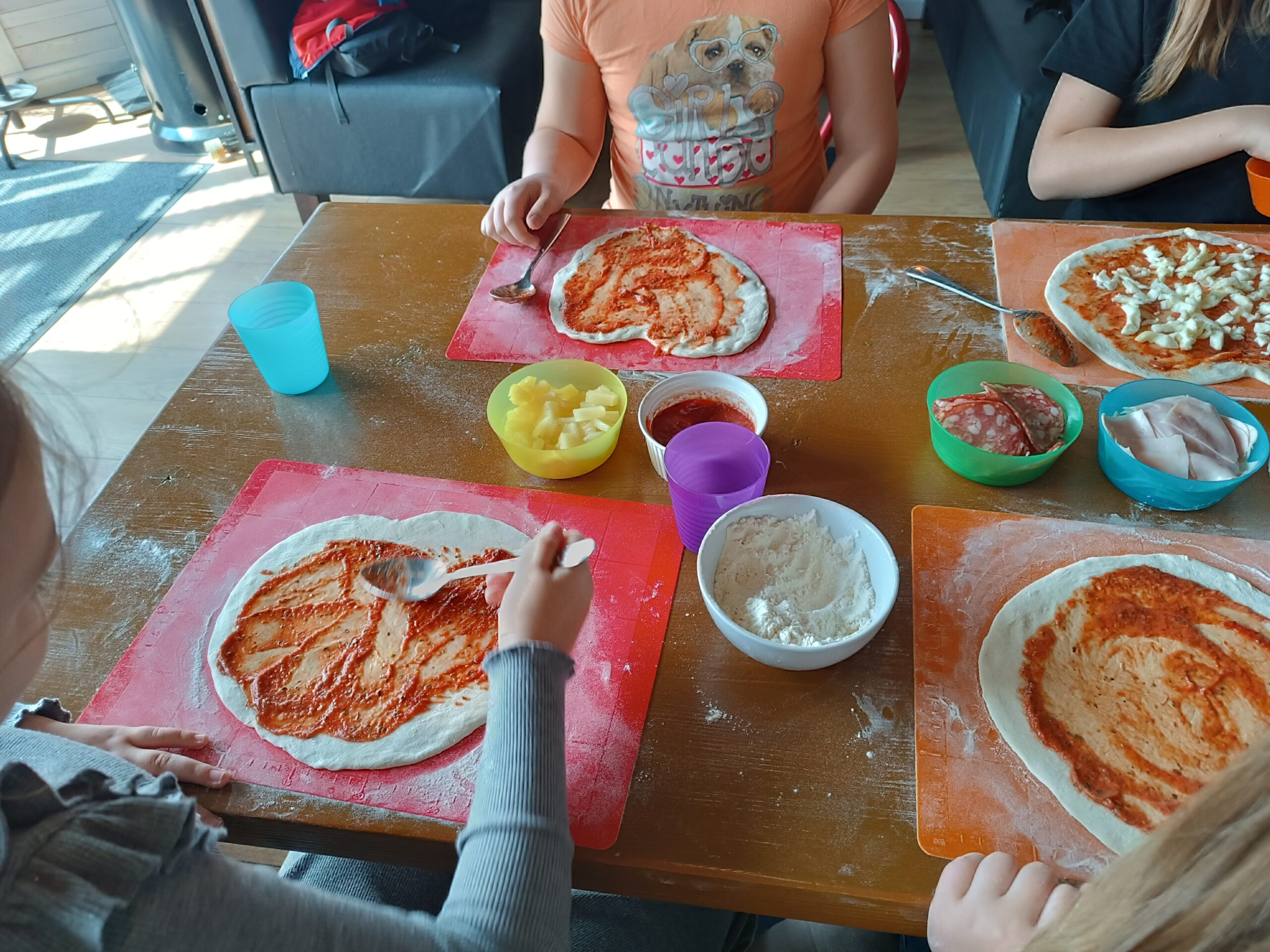  Na zdjęciu widać, jak dzieci rozsmarowują sos do pizzy na placku 