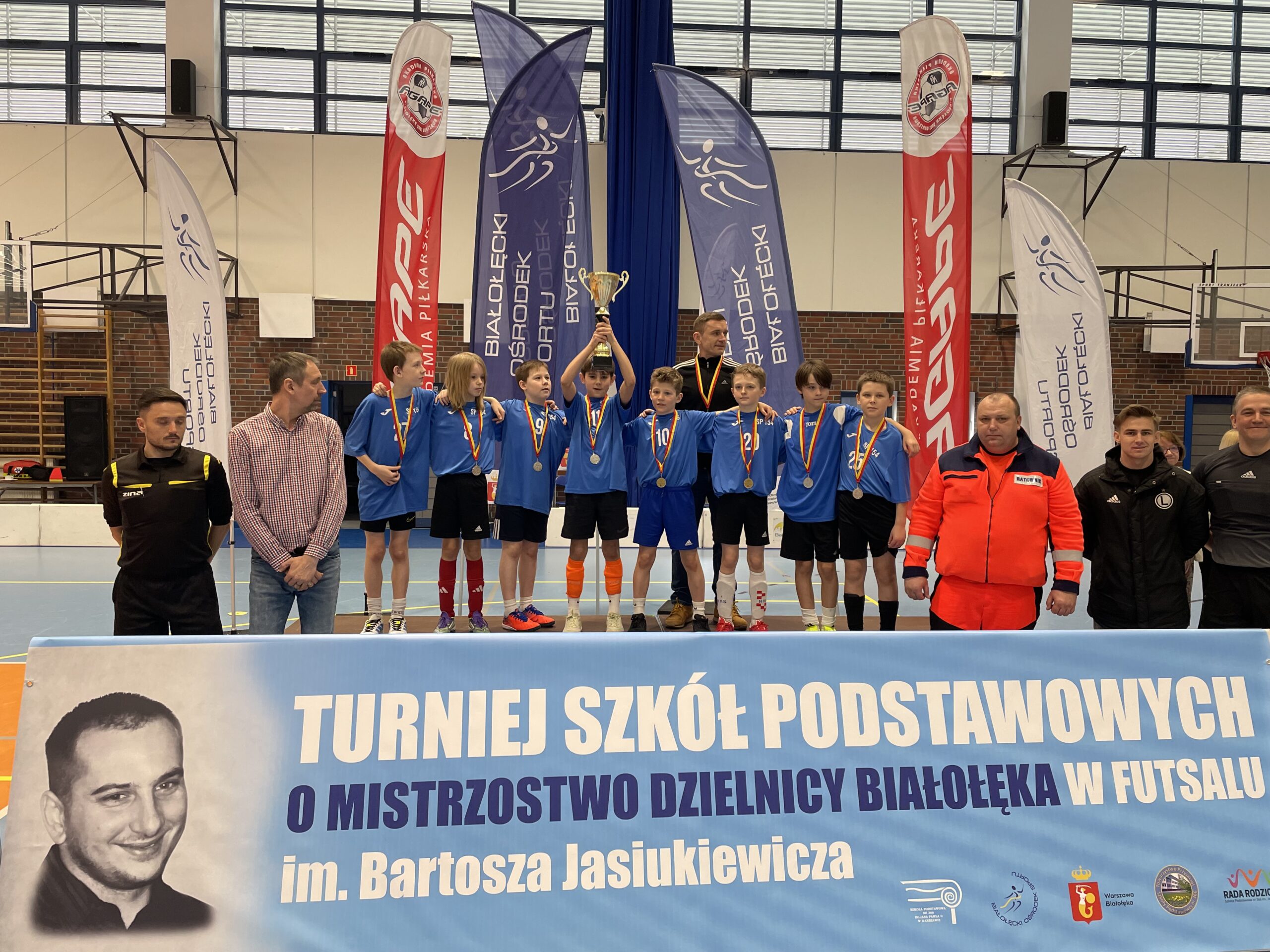 Chłopcy stoją na podium pod którym znajduję się nazwa turnieju