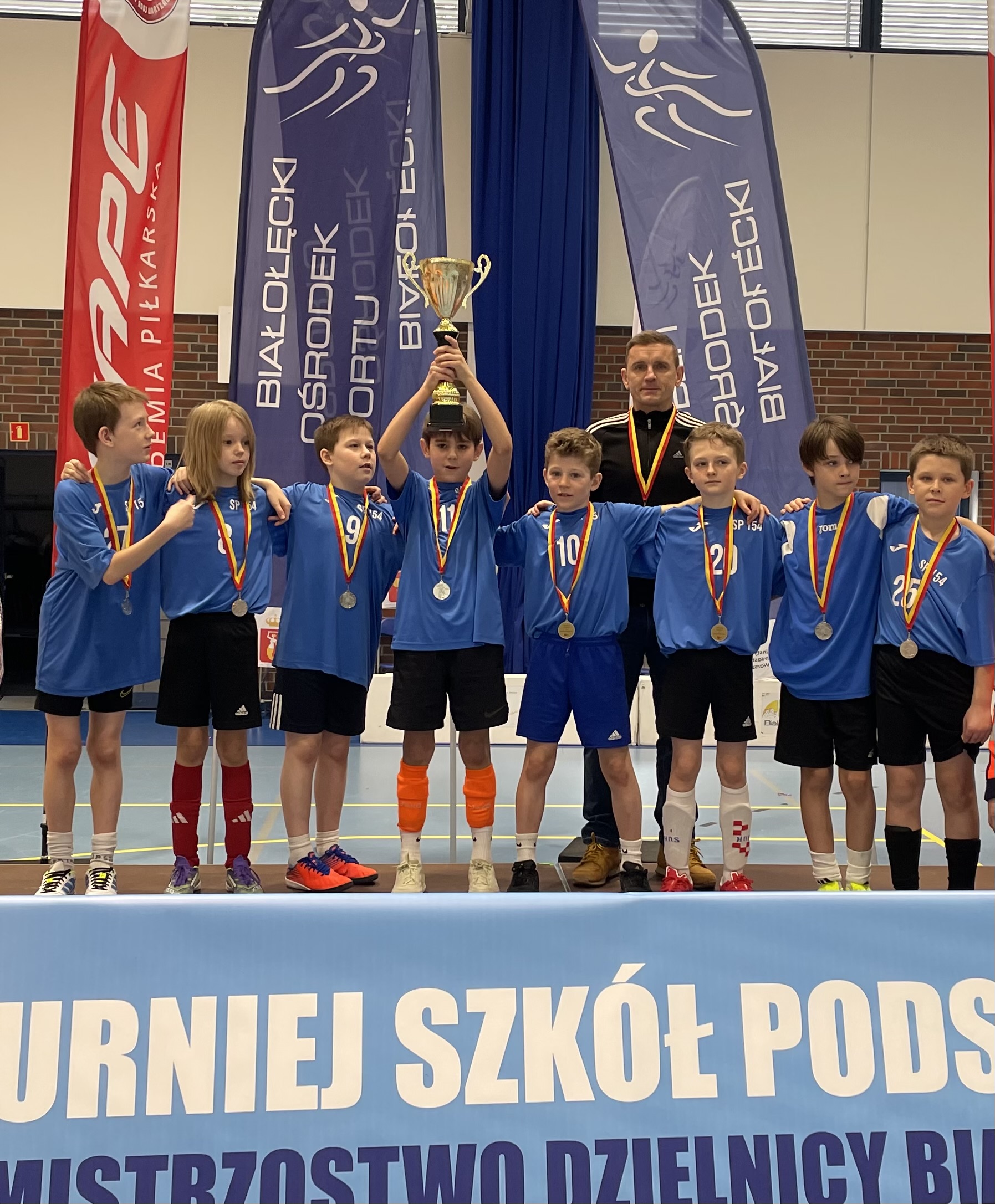 Chłopcy z medalami wznoszą puchar stojąc na podium