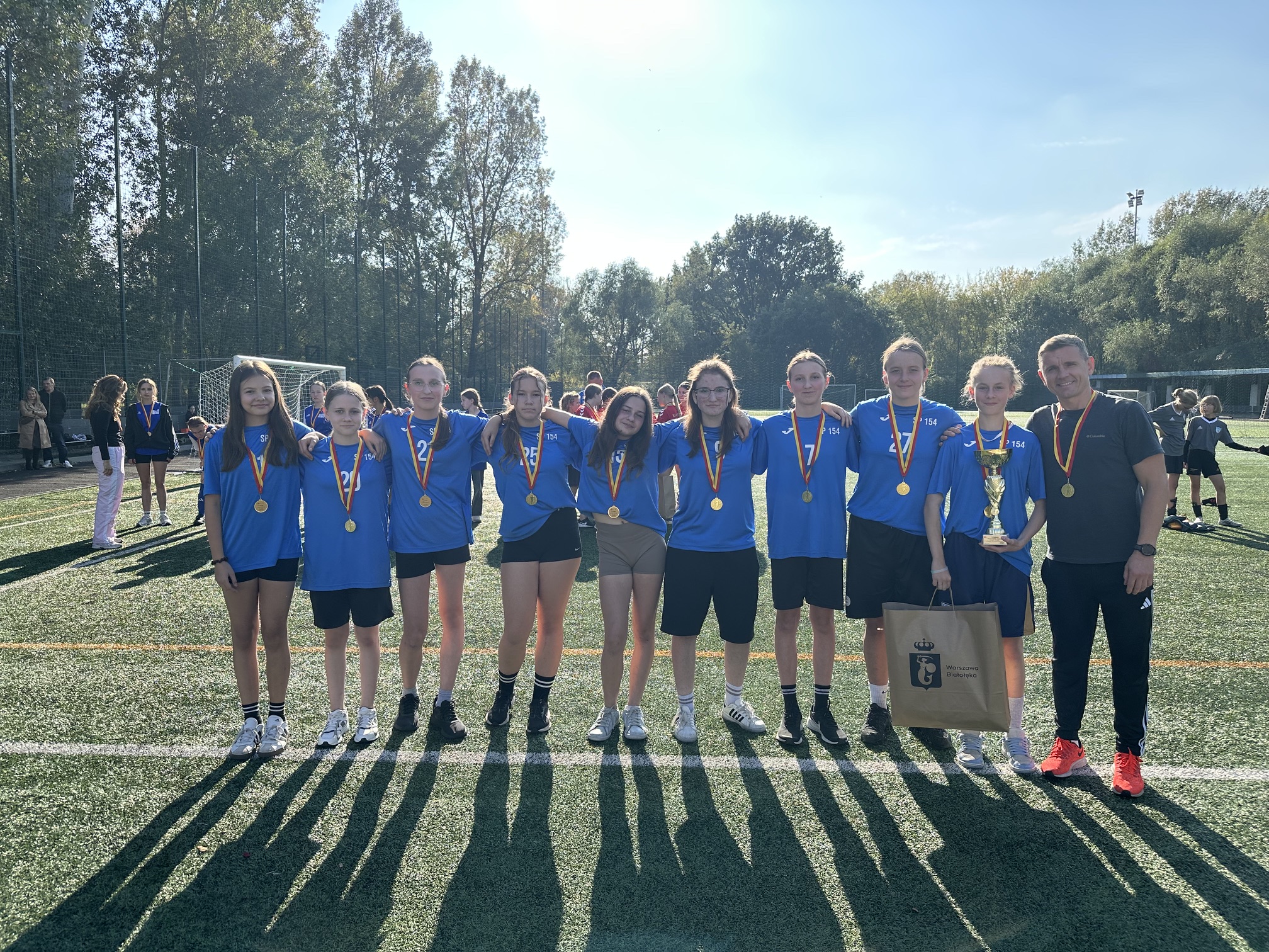 Dziewczyny stoją w szeregu z trenerem i złotymi medalami.